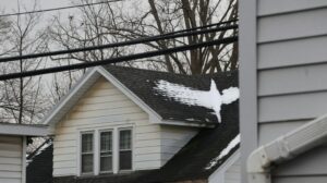 A residential roof with asphalt shingles, metal panels, and slate samples beside snow-covered eaves.